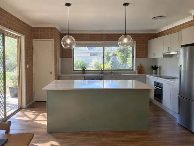Kitchen with two glass pendant lights over a large island, white cabinetry and brick walls in Swansea